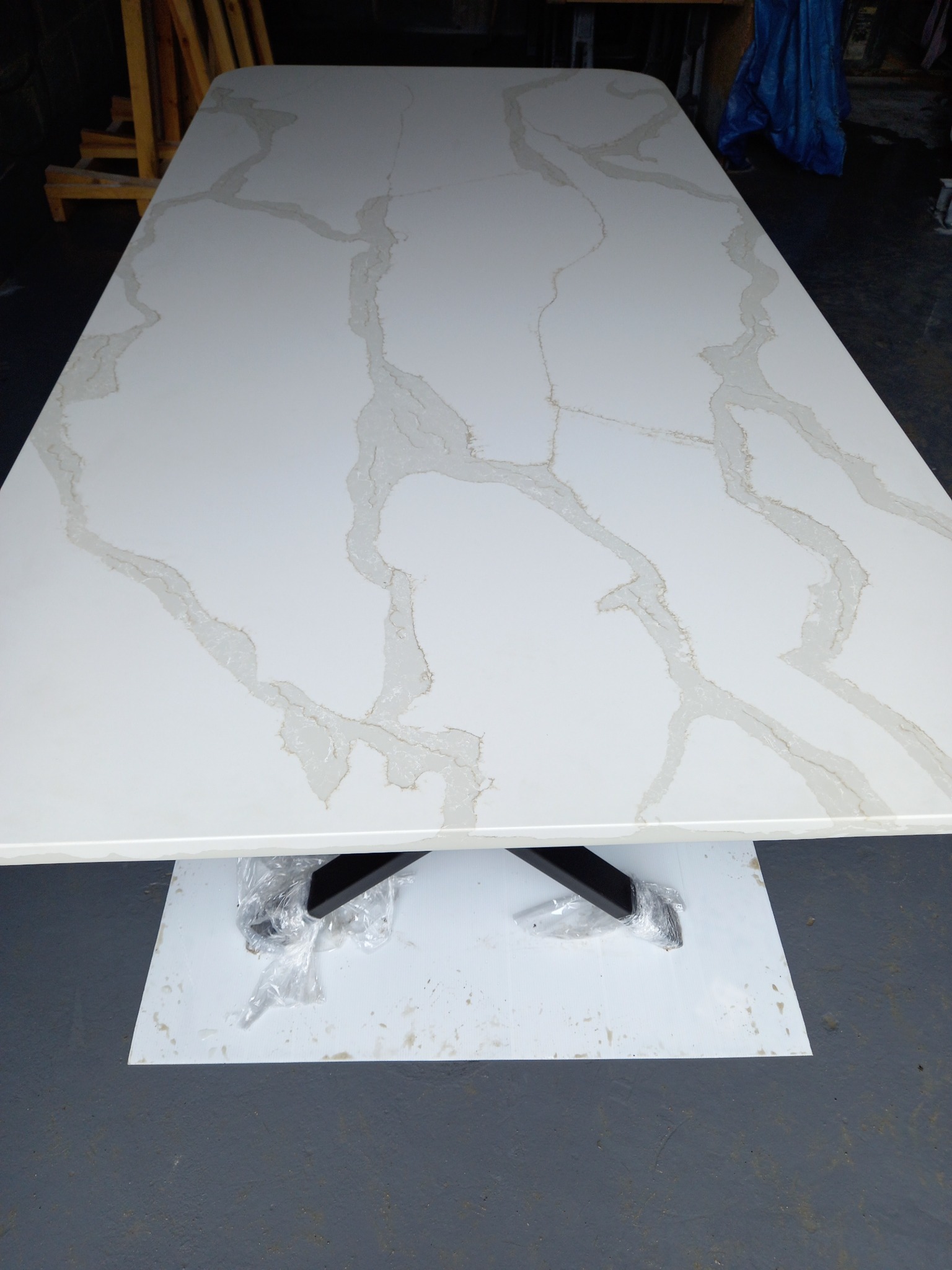 Biały blat stołu z wzorem marmuru, z czarnymi nogami jeszcze owiniętymi folią ochronną, ustawiony na białej płycie.