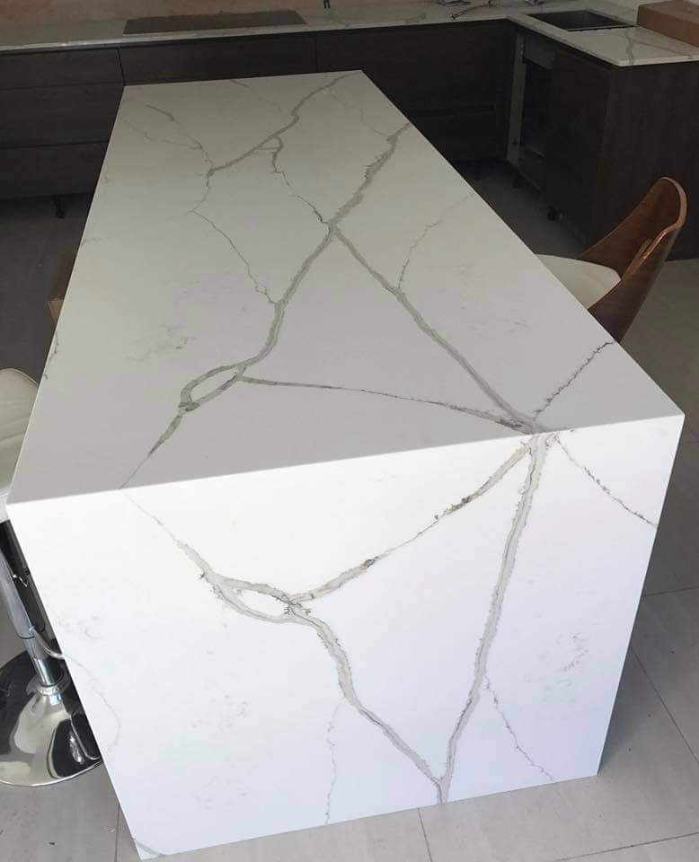 Biały blat kuchenny z szarymi żyłkami, widok z góry na wyspę kuchenną z krzesłami barowymi, minimalistyczny design.