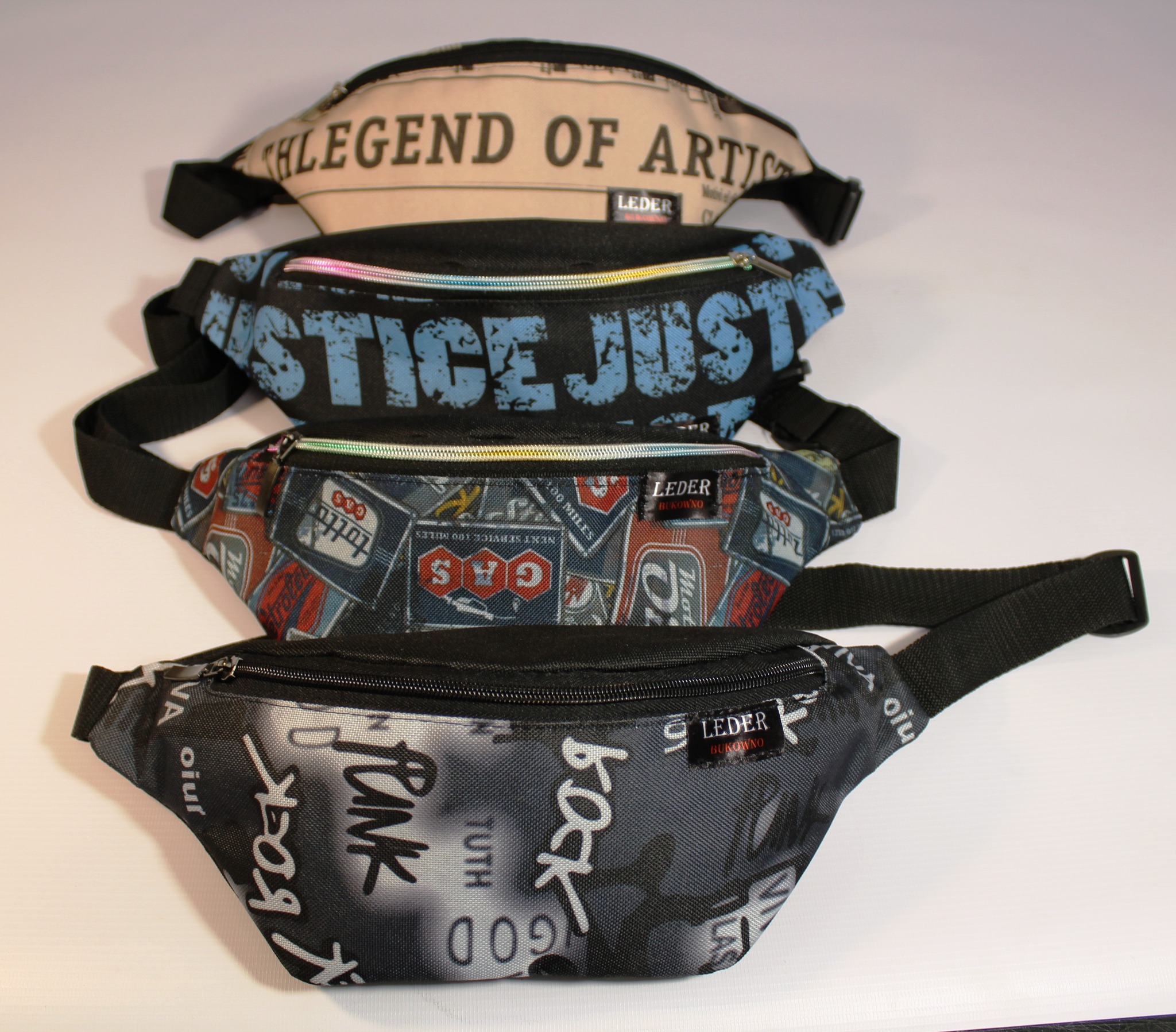 Stos czterech saszetek biodrowych z różnymi wzorami, w tym napisy 'LEGEND OF ARTIST', 'JUSTICE JUST' oraz motywy graficzne, widoczne logo producenta 'LEDER BUKOWNO'.