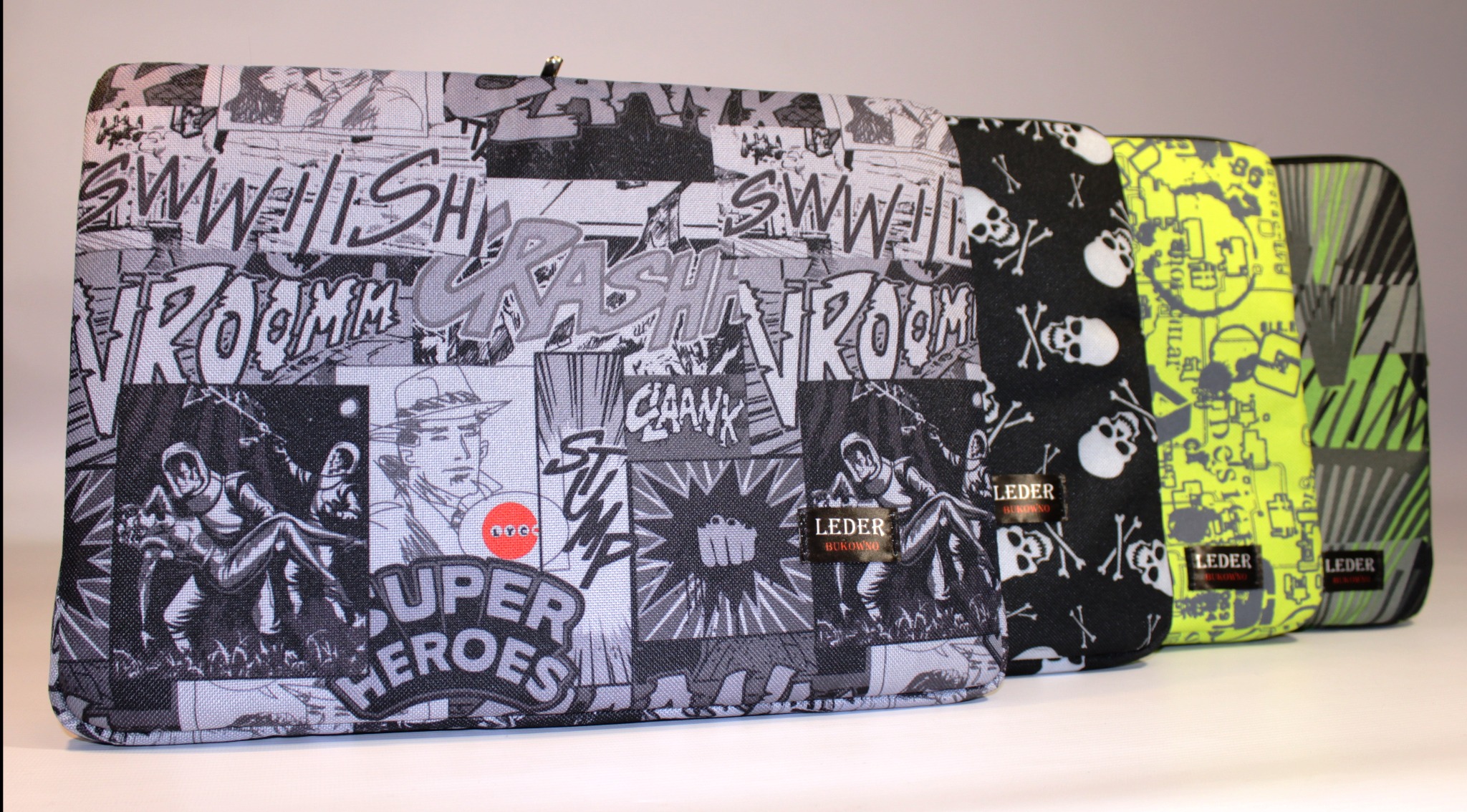 Rząd czterech pokrowców z różnymi wzorami: komiksowe motywy superbohaterów, czaszki, neonowe schematy i abstrakcyjne zielone linie, każdy z metką 'LEDER Bukowno'.