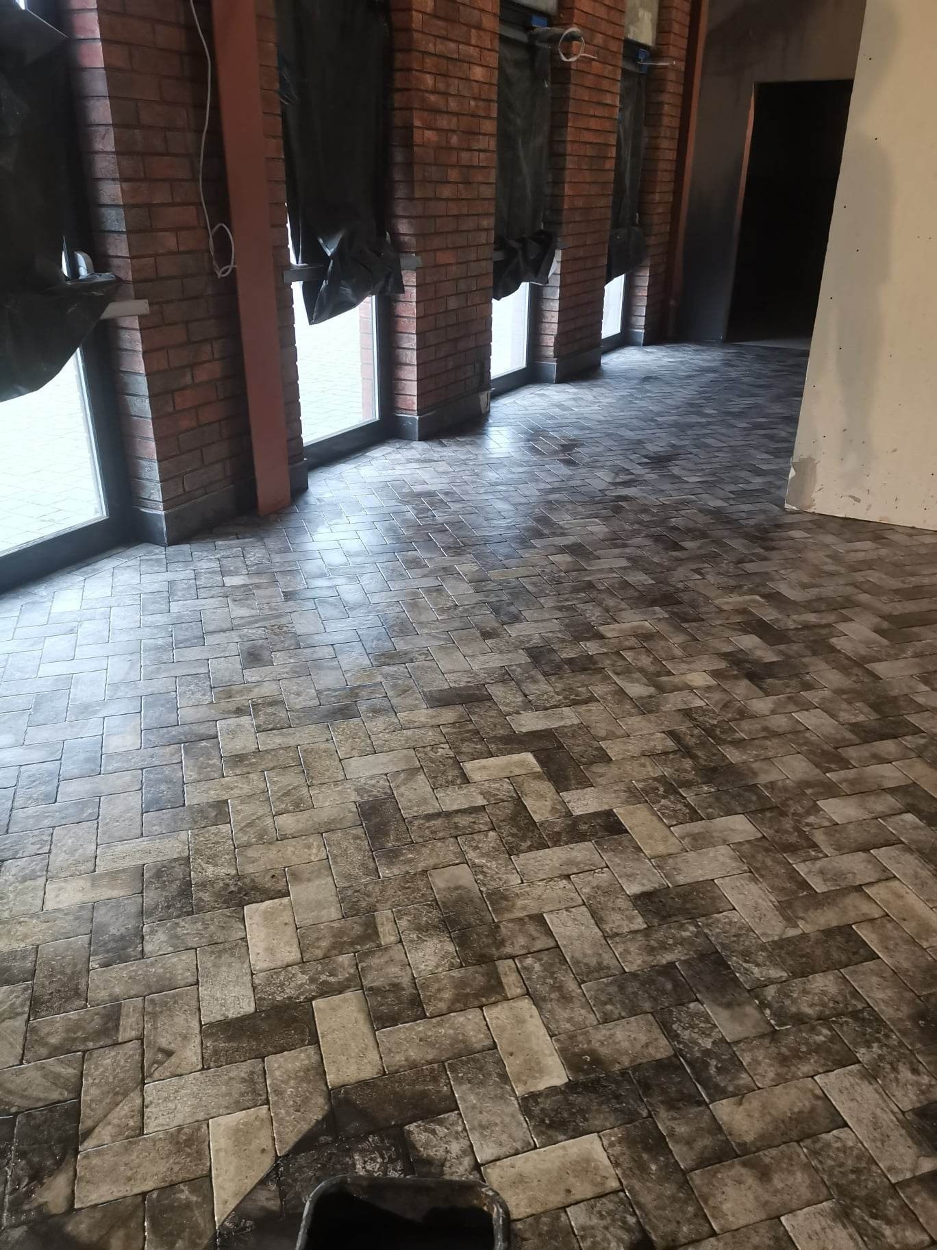 Ułożona kostka parkietowa w jodełkę w pomieszczeniu z ceglanymi filarami w Łodzi, widoczne ślady po fugowaniu.