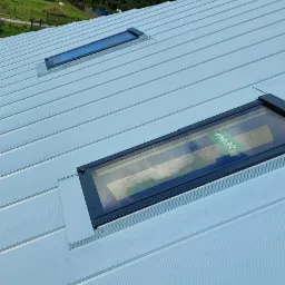 Jasnoszary dach z blachy trapezowej z dwoma oknami dachowymi Fakro, widok pod kątem.