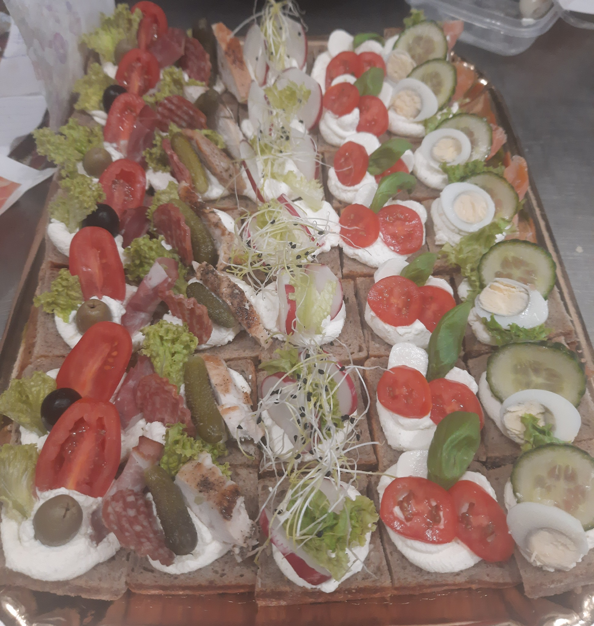 Taca z różnorodnymi kanapkami na ciemnym pieczywie, udekorowanymi kremowym serkiem, warzywami, wędlinami i jajkami przepiórczymi, przygotowana przez firmę cateringową z Częstochowy.