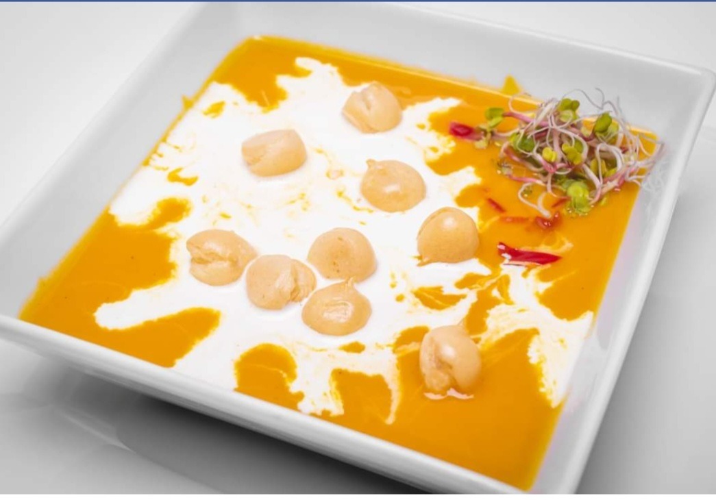 Krem z dyni w kwadratowym talerzu, z kleksami śmietany i kremowymi kluseczkami, udekorowany świeżymi kiełkami.