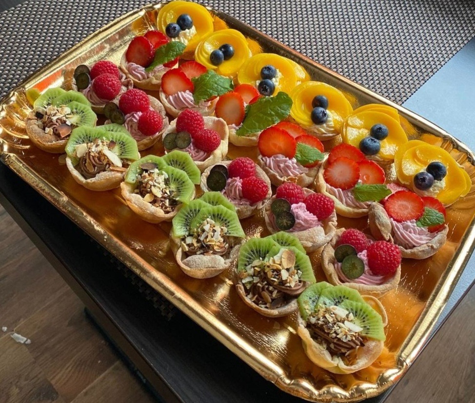Złota taca z mini tartaletkami z różnymi owocami: kiwi z posiekanymi migdałami, malinami i kremem, truskawkami i miętą, brzoskwiniami i borówkami.