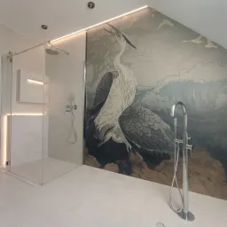 Nowoczesna łazienka z kabiną prysznicową, chromowaną armaturą i tapetą przedstawiającą żurawie na tle drzew i fal.