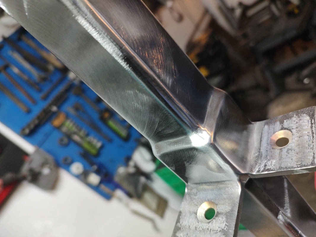 Szlifowany element konstrukcyjny ze stali nierdzewnej z nawierconymi otworami, widoczne narzędzia warsztatowe w tle.