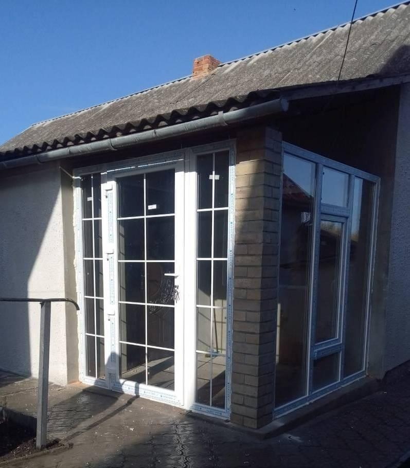 Zadaszone wejście do domu z białymi ramami okiennymi z podziałami, wykończone cegłą, widok z zewnątrz.