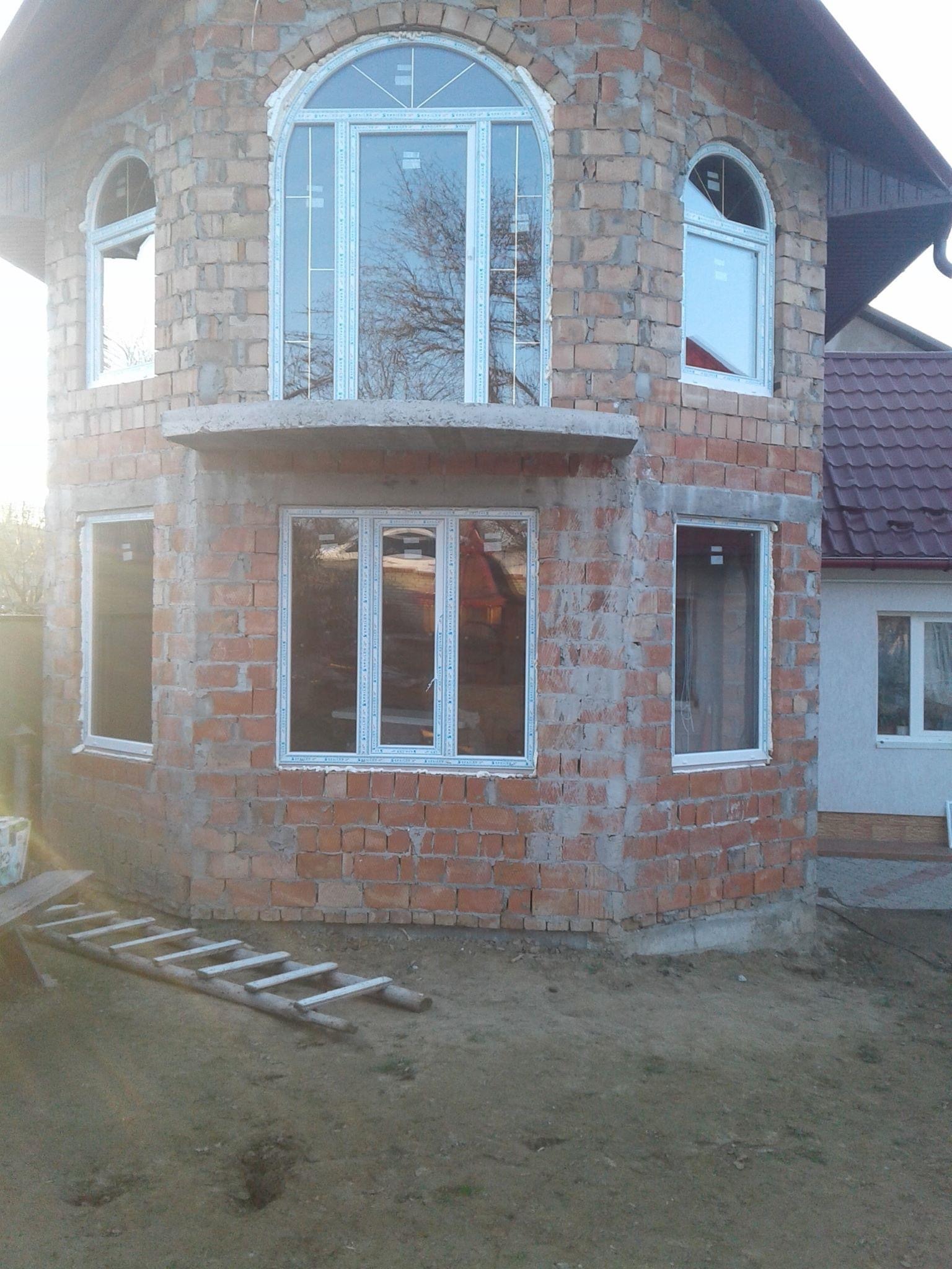 Surowy stan budynku z czerwonej cegły z zamontowanymi białymi oknami, widoczne okna łukowe na górze i drabina oparta o ścianę.