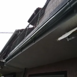 Szare rynny zamontowane na balkonie budynku mieszkalnego, widoczne z dołu pod kątem, z anteną na dachu w tle.