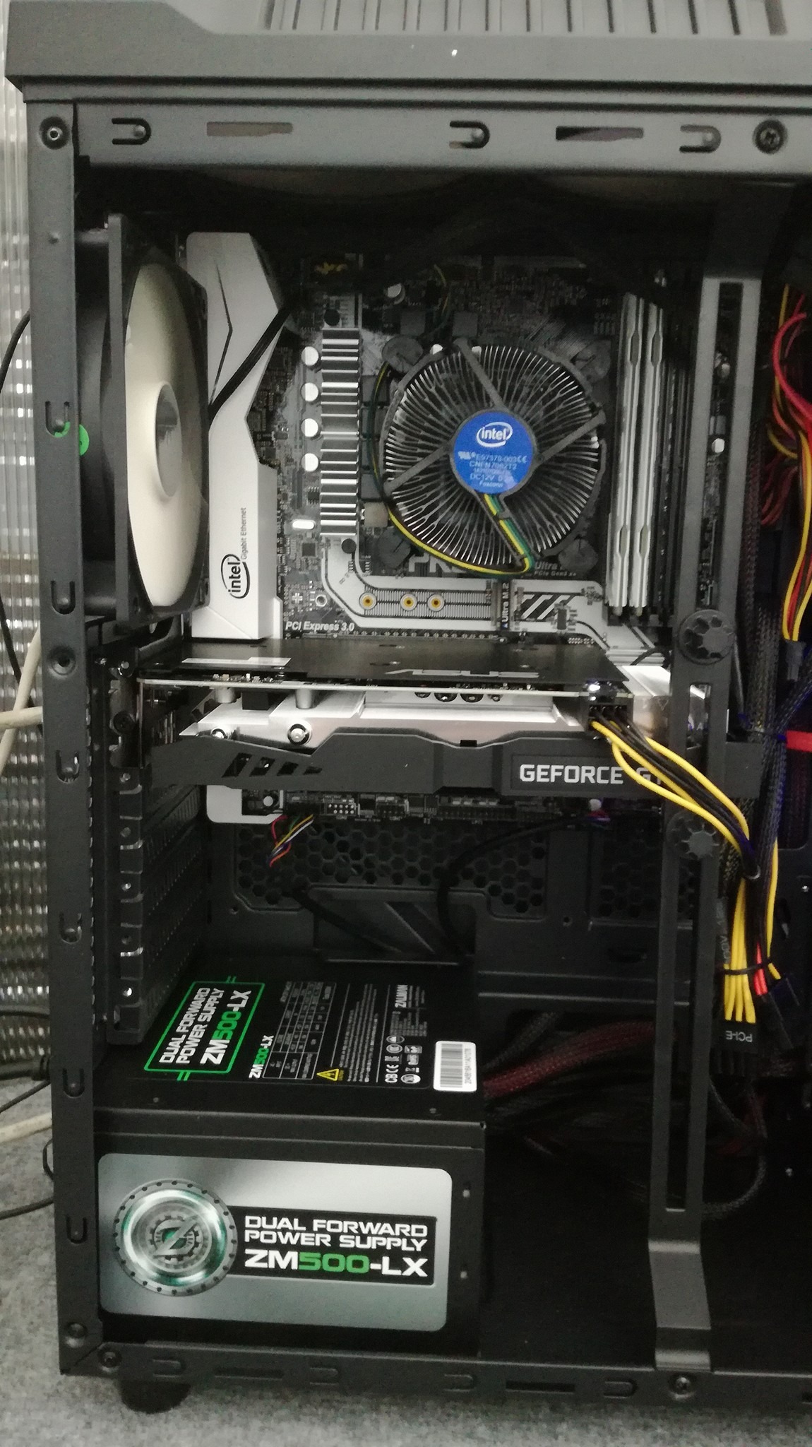 Wnętrze obudowy komputera stacjonarnego z widoczną płytą główną, kartą graficzną GeForce, zasilaczem ZM500-LX oraz chłodzeniem procesora Intel. Widoczne kable zasilające w kolorach żółtym i czarnym.