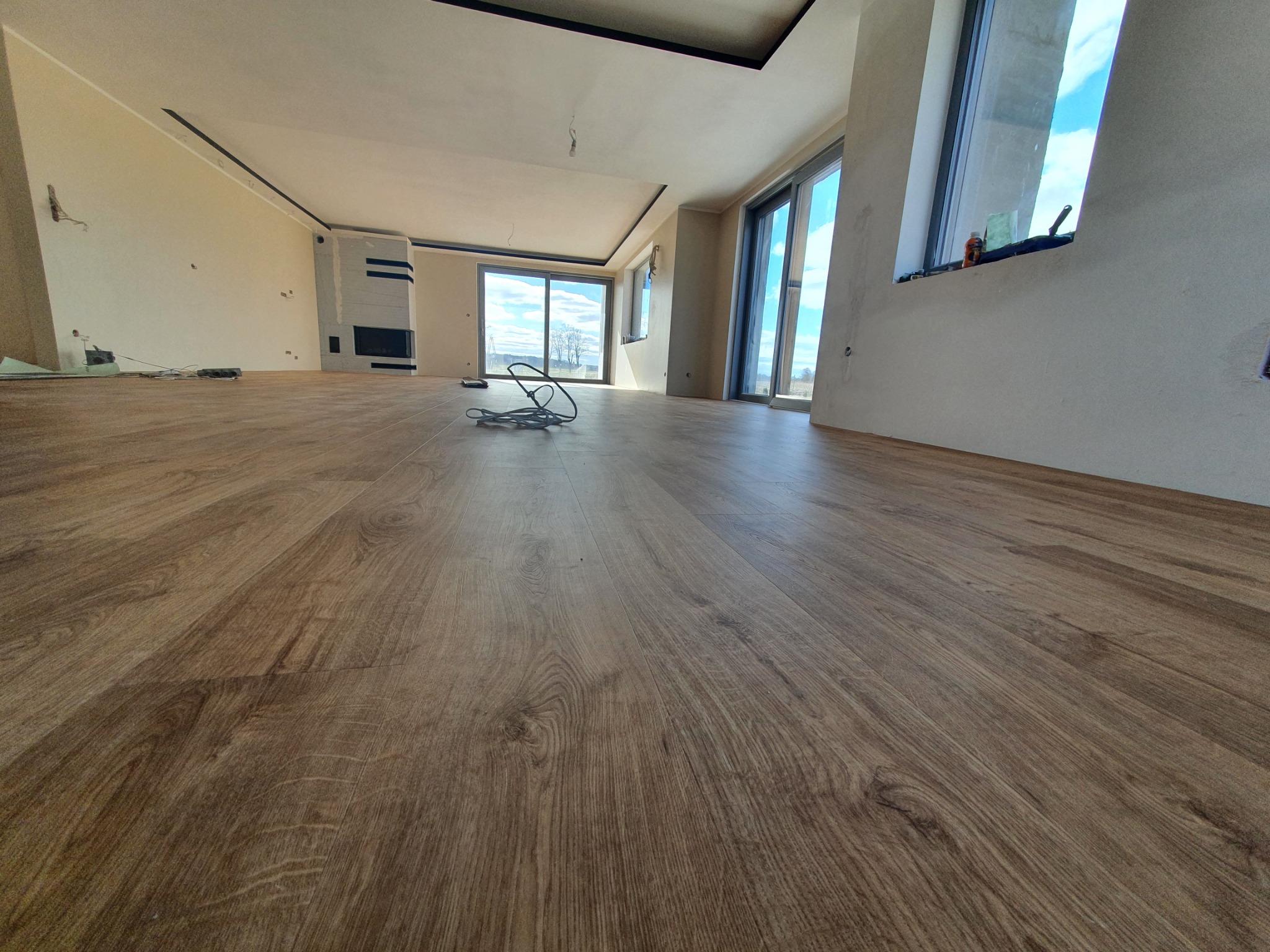 Salon w trakcie wykańczania, z nową podłogą imitującą drewno, widoczne kable i elementy wykończeniowe ścian.