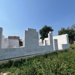 Coreltb Builders Sp. z o.o. - Wznoszenie ścian parteru domu z białych bloczków betonu komórkowego Ytong. Widoczne zbrojenia i fragmenty deskowania. W tle zieleń i błękitne niebo.