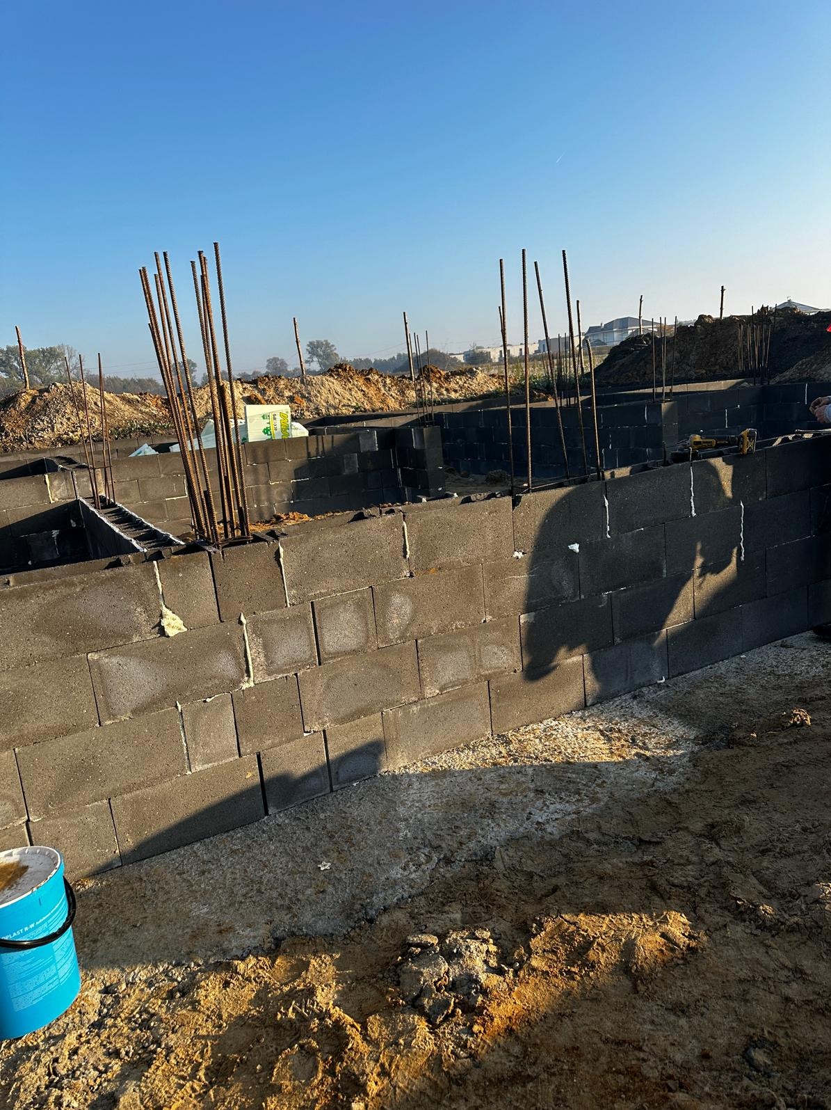 Wznoszenie fundamentów z bloczków betonowych z wystającymi prętami zbrojeniowymi w Jaworznie, widoczny fragment ściany i grunt pod budowę.