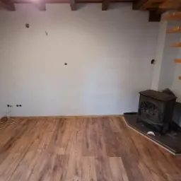 Wykończony pokój z panelami podłogowymi w odcieniach brązu, drewnianymi schodami i żeliwnym piecem.