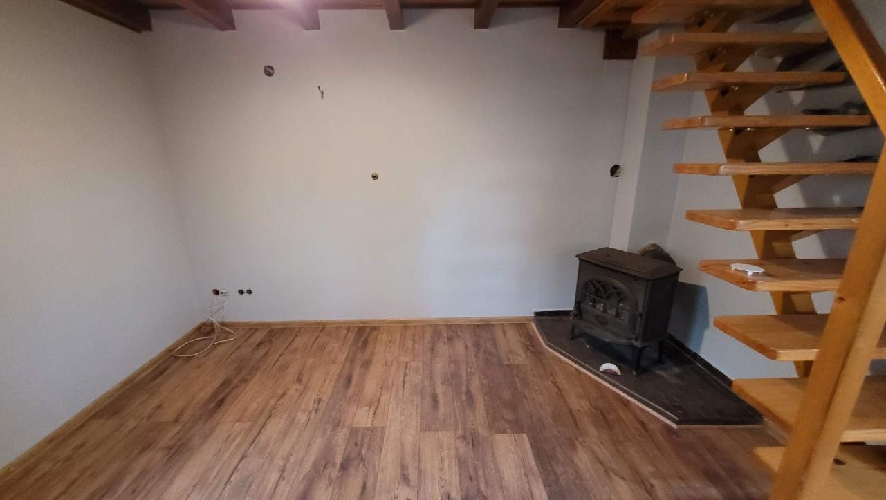 Wykończony pokój z panelami podłogowymi w odcieniach brązu, drewnianymi schodami i żeliwnym piecem.