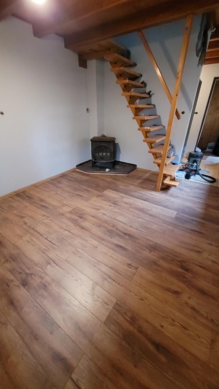 Ułożone panele podłogowe w pokoju z drewnianymi schodami i piecem typu koza.