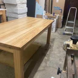 Arkadiusz Żołnowski - Rozłożony drewniany stół z blatem o jasnym odcieniu drewna, widoczny w warsztacie stolarskim z narzędziami i materiałami w tle.