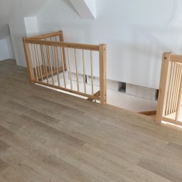 Arkadiusz Żołnowski - Drewniana balustrada schodów na poddaszu z jasną podłogą panelową, widoczne otwory w ścianie pod schodami.