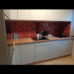 Arkadiusz Żołnowski - Nowoczesna kuchnia z szarymi szafkami i drewnianym blatem, ściana nad blatem wykończona motywem czerwonej cegły.