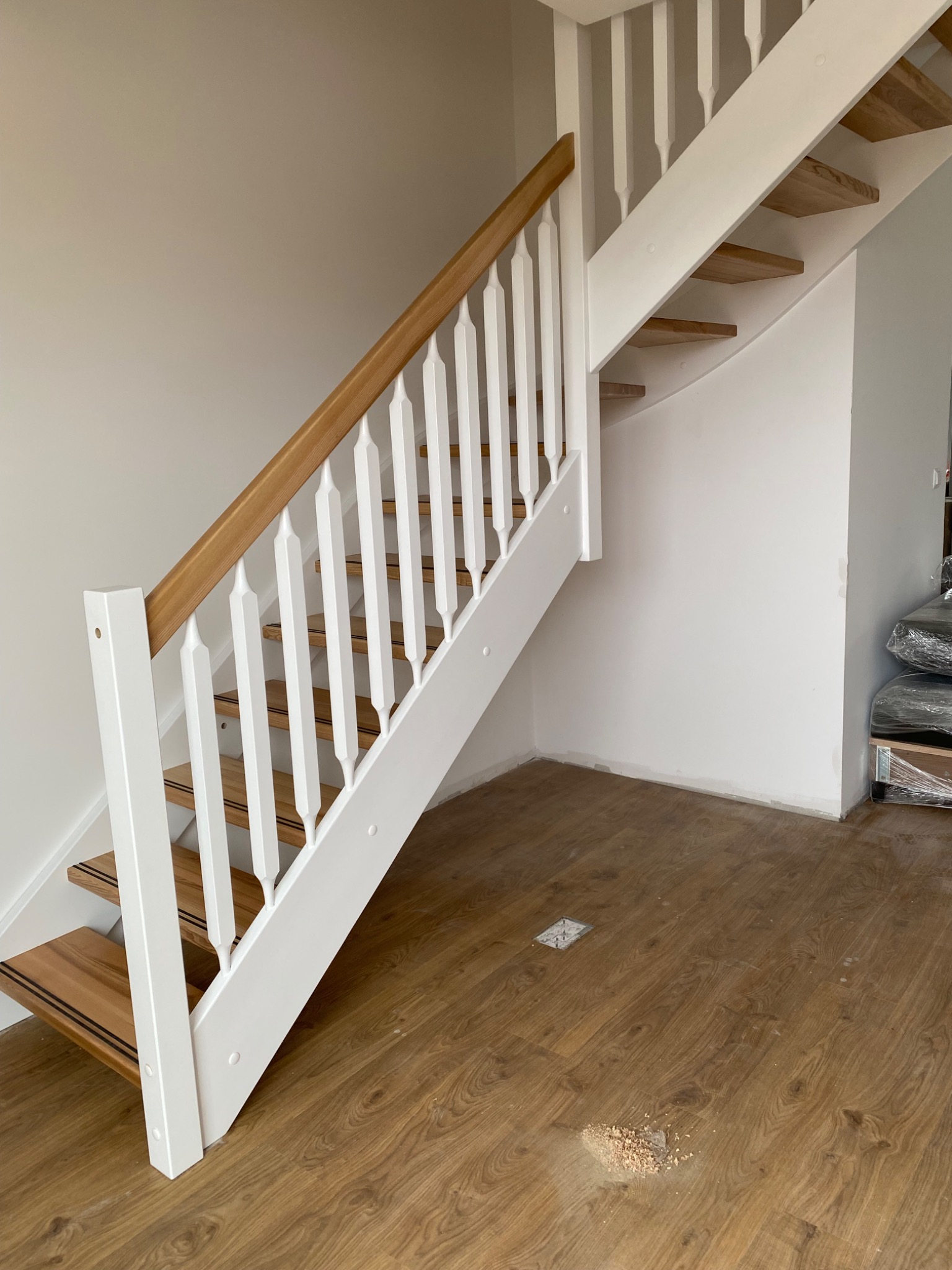 Nowoczesne schody z drewnianymi stopniami i białą balustradą, widoczne w jasnym wnętrzu, z drewnianą podłogą i minimalistycznym wykończeniem ścian.