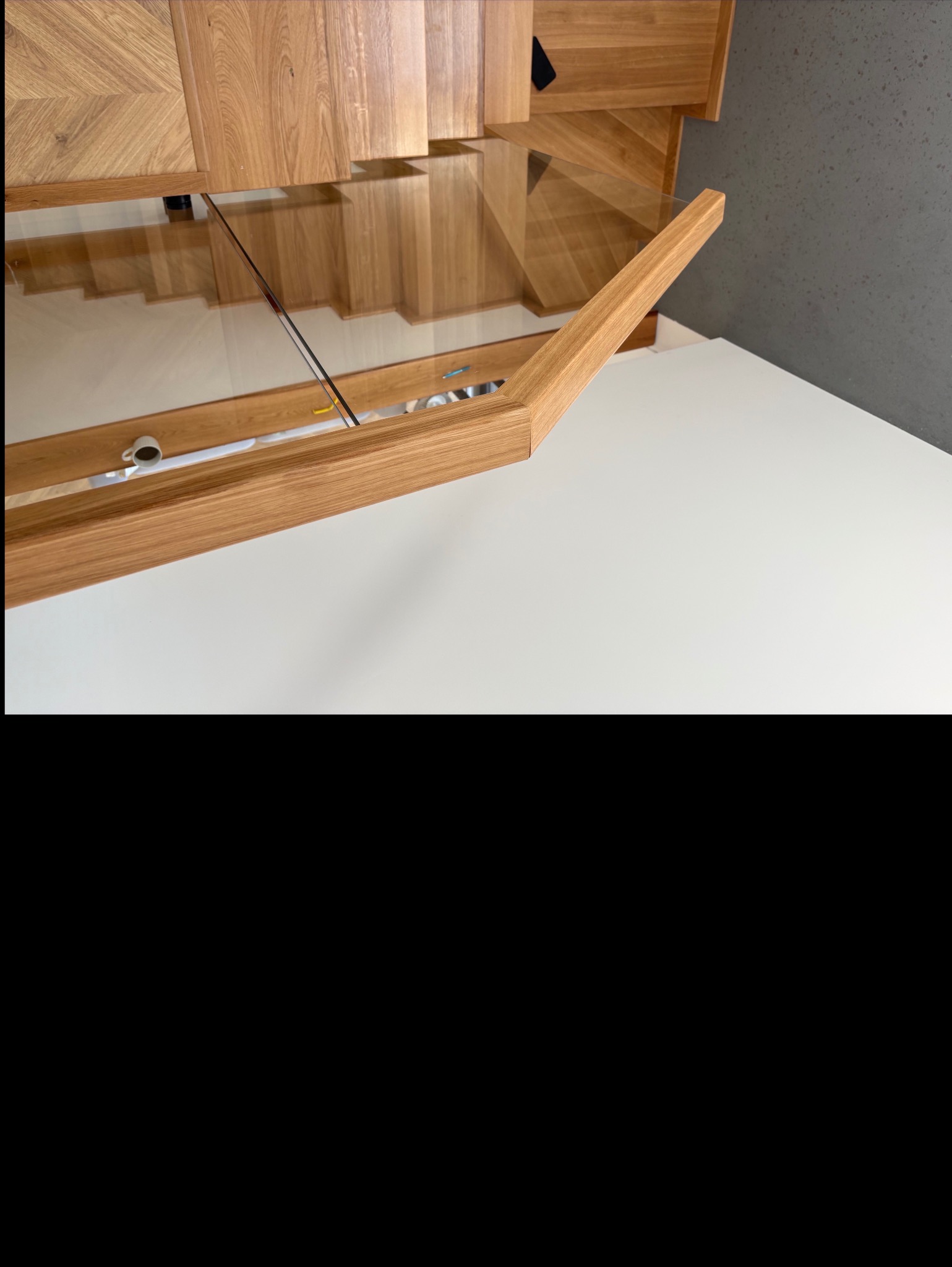 Otwarta szafka dębowa z blatem i szklaną półką, widoczna filiżanka. Dekoracyjne wykończenie frontów. Ujęcie z góry, z bliska.