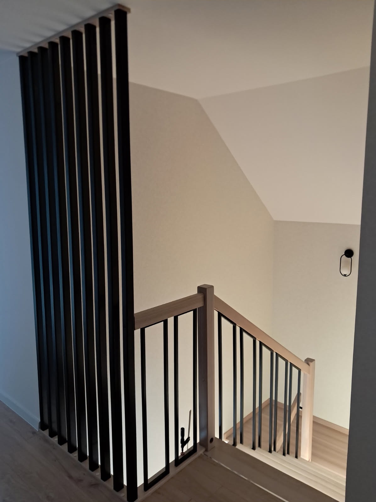 Nowoczesne schody z jasnego drewna z czarnymi balustradami i pionowymi elementami dekoracyjnymi, widok z góry, minimalistyczny design.