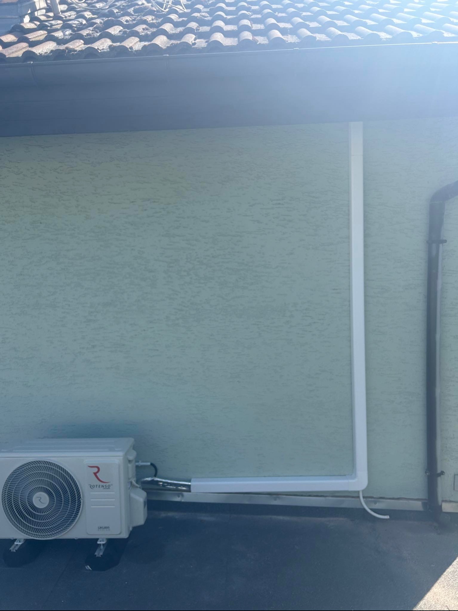 Zewnętrzna jednostka klimatyzatora marki Rotenso zamontowana na elewacji budynku z widocznymi rurami w białej listwie maskującej.