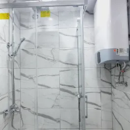 Nowoczesna kabina prysznicowa z chromowanymi elementami i marmurowymi płytkami, widoczny biały bojler elektryczny.