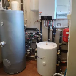 Instalacja kotła gazowego Viessmann z dwoma zasobnikami wody, widoczne liczne rury i zawory, całość w pomieszczeniu z brązowymi płytkami podłogowymi.