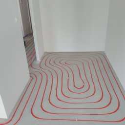 W.R. Silver System - Czerwone rurki układane spiralnie na szarym podłożu w trakcie montażu systemu ogrzewania podłogowego w jasnym pomieszczeniu.