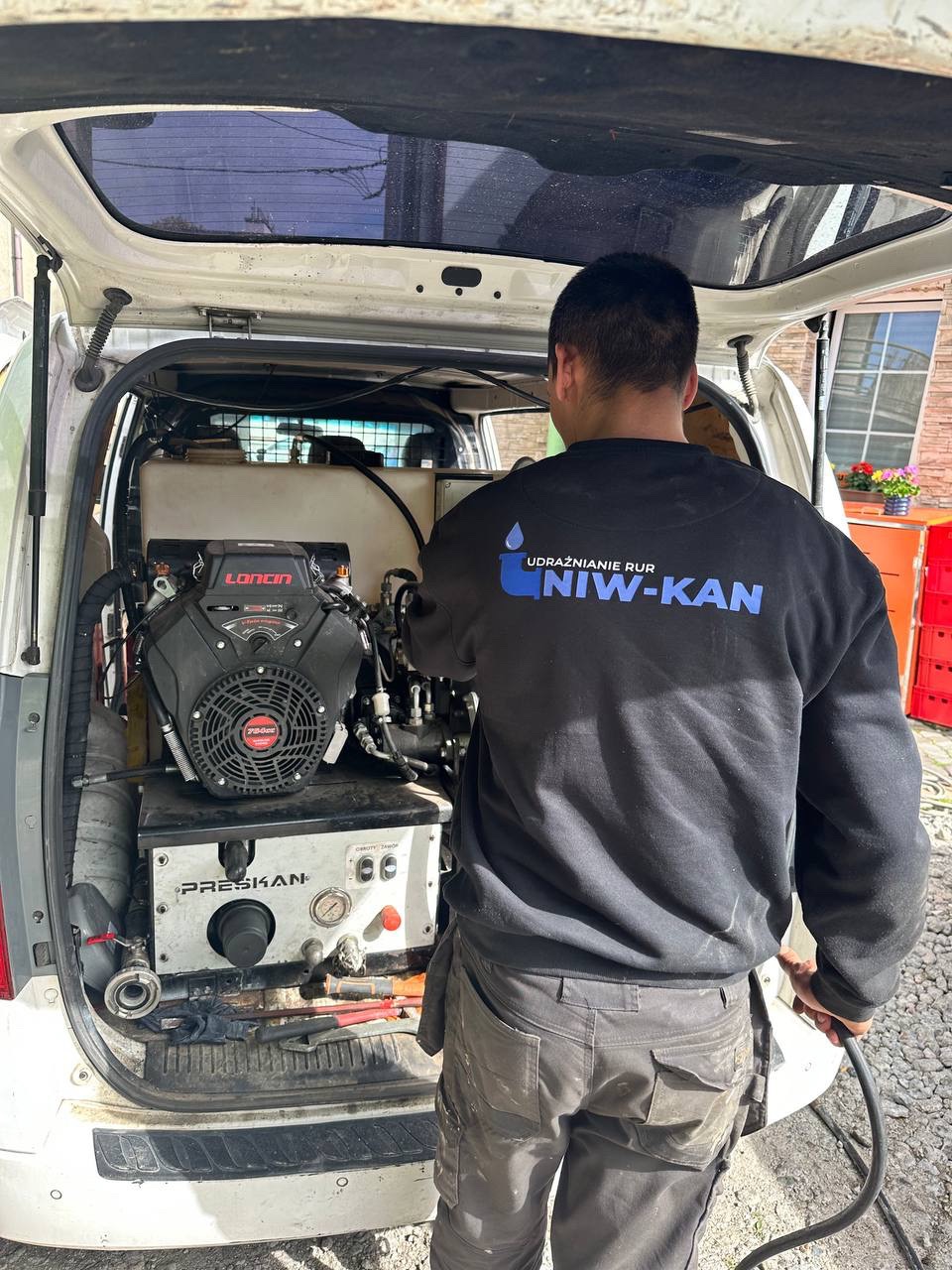 Sprzęt do udrażniania rur w samochodzie serwisowym firmy z Sosnowca. Widoczny pracownik w uniformie z logo firmy. Specjalistyczne narzędzia i wyposażenie.