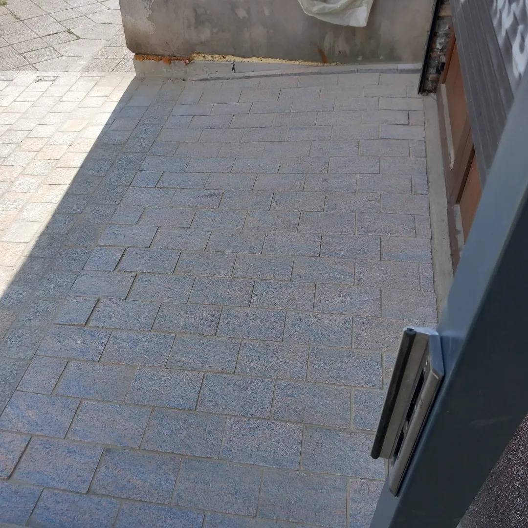 Szczegółowe ujęcie szarej kostki brukowej ułożonej przy ścianie budynku w Szczecinie, widoczne delikatne różnice w odcieniach poszczególnych elementów.