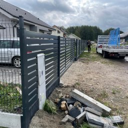 Superpłot - Nowoczesne, grafitowe ogrodzenie panelowe z bramą przesuwną, widok z zewnątrz posesji, z dostawczym autem w tle. Częściowo ukończony montaż.