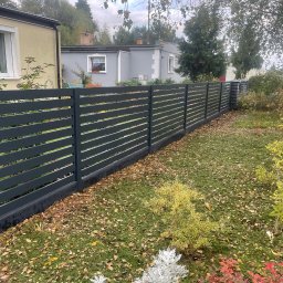 Superpłot - Nowoczesne, poziome ogrodzenie panelowe w kolorze grafitowym, oddzielające posesję z domem w tle. Jesienne liście na trawie dodają koloru.