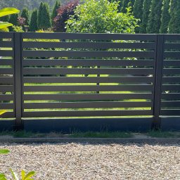 Superpłot - Nowoczesne, poziome ogrodzenie panelowe w kolorze grafitowym, z widokiem na zielony trawnik i drzewa w tle. Minimalistyczny design i staranne wykonanie.