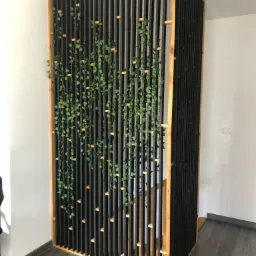 Drewniana ażurowa ścianka działowa w czarnym kolorze z elementami naturalnego drewna, ozdobiona pnącą zielenią, oddzielająca schody od reszty pomieszczenia.