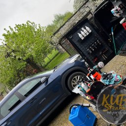 Patryk Kubulus usługi KubiSteamer - Mobilna myjnia parowa: Niebieski SUV, otwarte drzwi bagażnika z uporządkowanym zestawem środków czyszczących i narzędzi, wózek z akcesoriami do czyszczenia tapicerki, logo firmy Kubi Steamer...