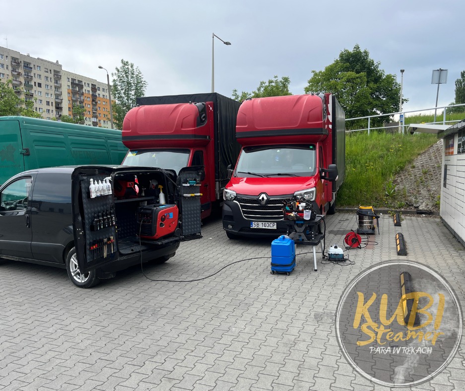 Dwa czerwone busy z wysoką kabiną oraz czarny van z otwartym tyłem, wyposażony w narzędzia i generator, na parkingu podczas świadczenia usługi czyszczenia parowego. W tle budynki mieszkalne i zieleń.