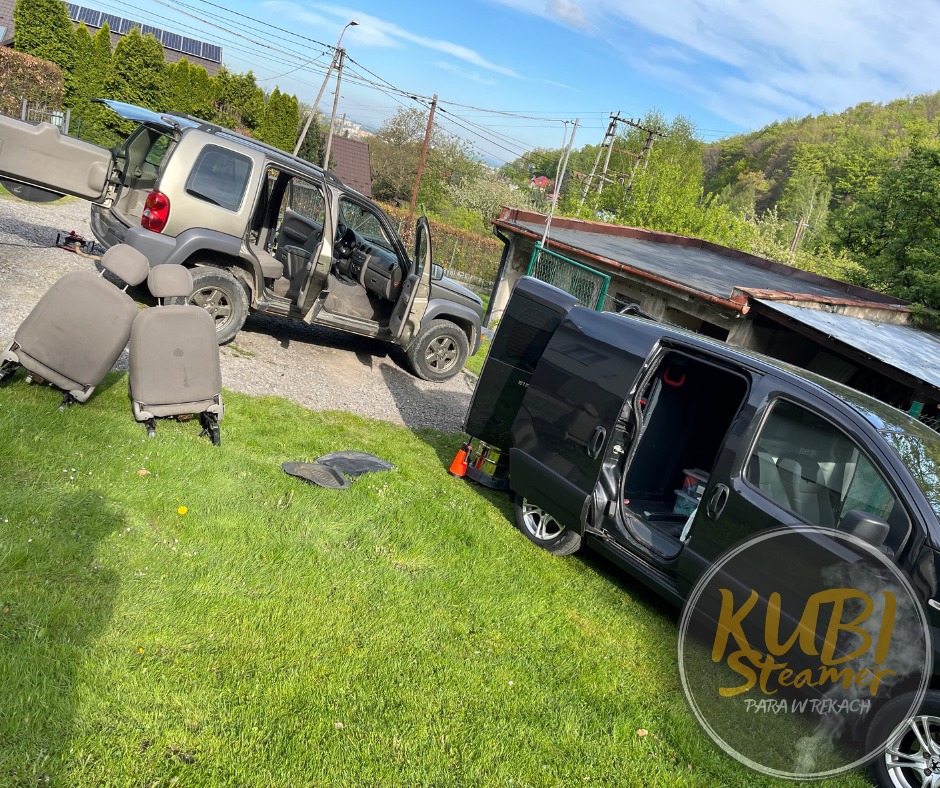 Dwa samochody na trawie, z wyjętymi fotelami samochodowymi obok; jeden samochód osobowy z otwartymi drzwiami i bagażnikiem, drugi to czarny van z otwartymi drzwiami, widoczne logo firmy nałożone...