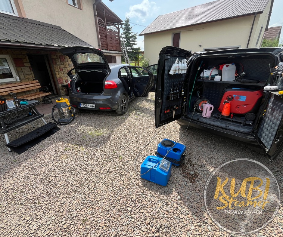 Mobilna usługa czyszczenia: Szary samochód z otwartym bagażnikiem obok czarnego auta dostawczego z otwartymi drzwiami, ukazującymi wyposażenie do czyszczenia, w tle dom z kamienną elewacją...