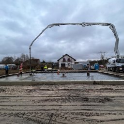 Firma budowlana Domy Raz Dwa - Wylewanie betonu na przygotowany fundament pod budowę domu jednorodzinnego; widoczny betonowóz z pompą, pracownicy w odblaskowych kamizelkach i szalunek.