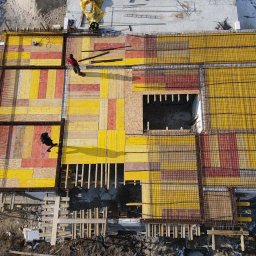 Firma budowlana Domy Raz Dwa - Widok z góry na plac budowy z przygotowanymi szalunkami i zbrojeniami fundamentów domu, z widocznymi pracownikami i elementami konstrukcyjnymi.