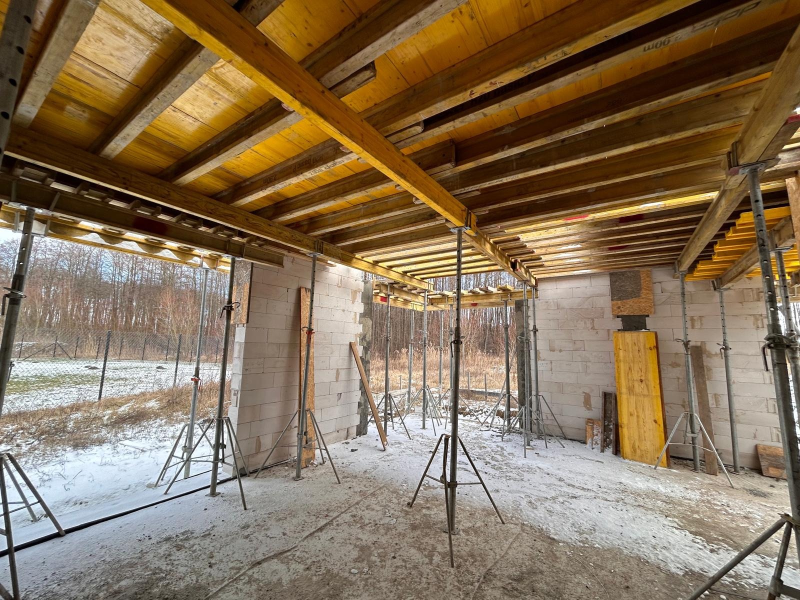 Wnętrze powstającego domu murowanego w Toruniu w stanie surowym otwartym, widoczne ściany z bloczków, drewniane szalunki stropu podparte metalowymi stemplami, śnieg na podłodze.