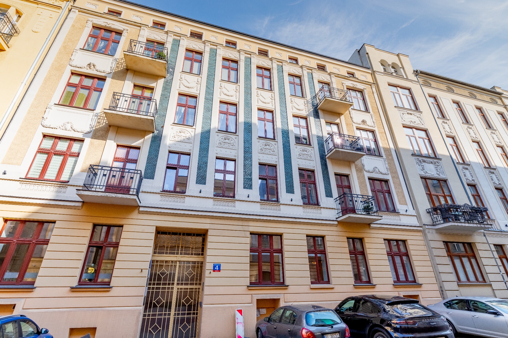 Elewacja kamienicy z balkonami i czerwonymi ramami okiennymi, widok z dołu na błękitne niebo.