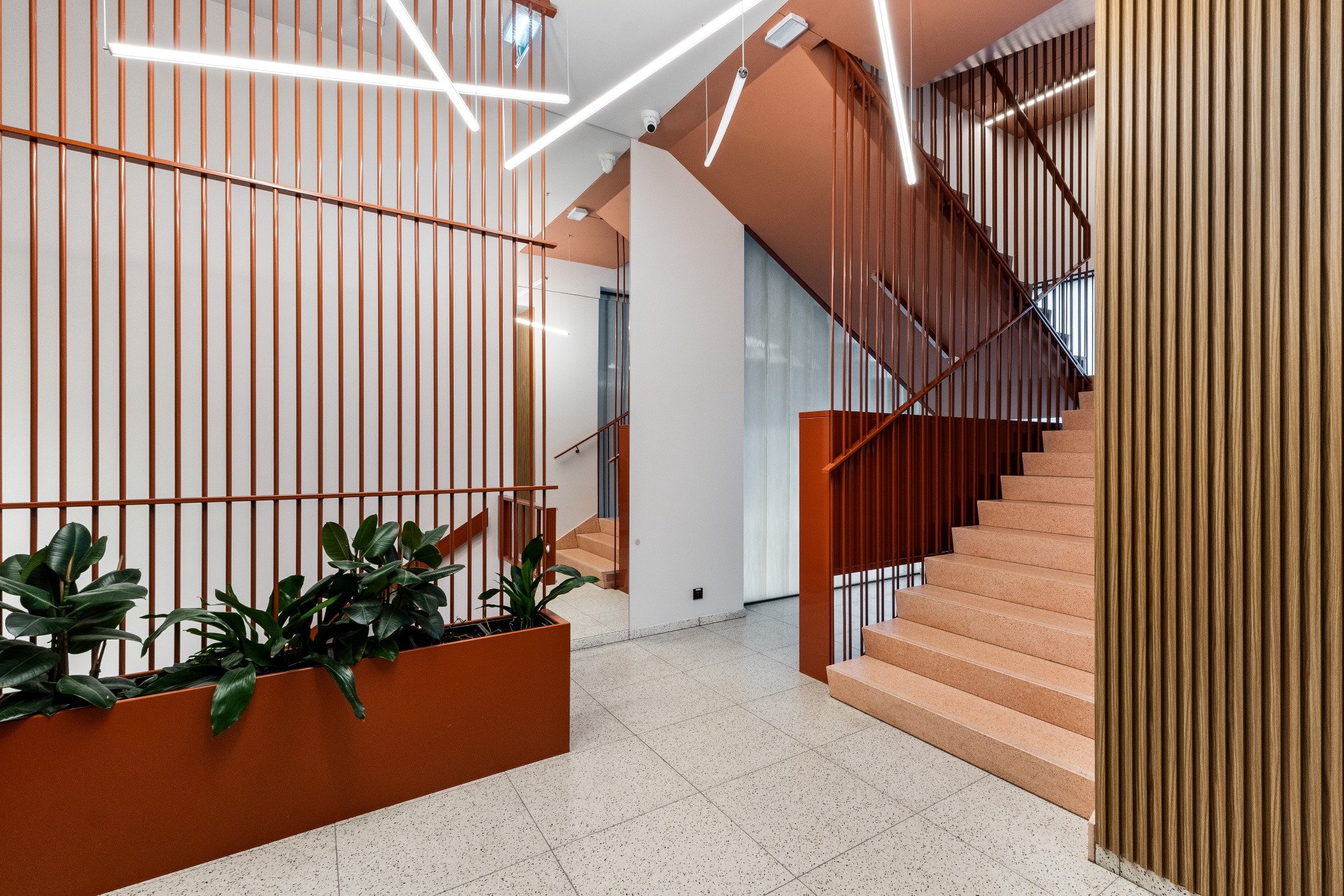 Klatka schodowa w nowoczesnym budynku z terazzo, z roślinami w donicy i geometrycznym oświetleniem LED.
