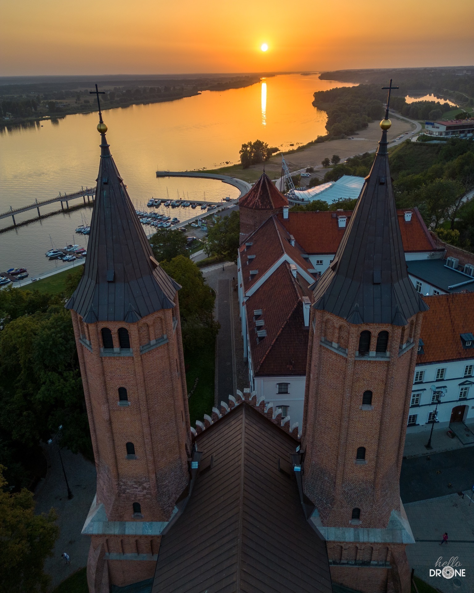 Panorama z lotu ptaka na katedrę z cegły z dwiema wieżami, rzekę z mostem i mariną o zachodzie słońca.