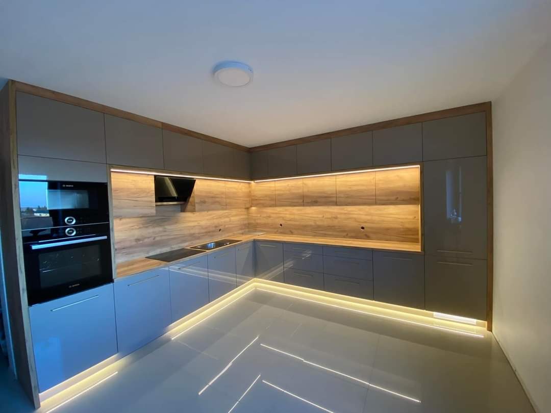 Nowoczesna kuchnia na wymiar z szarymi frontami, drewnianym panelem ściennym i oświetleniem LED podszafkowym oraz przypodłogowym.