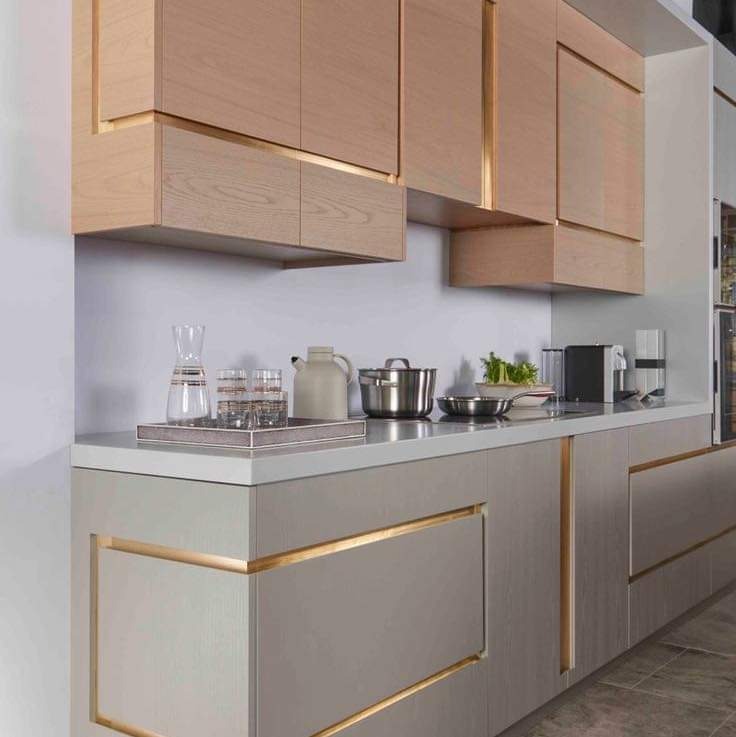 Nowoczesna kuchnia z drewnianymi szafkami górnymi i szarymi dolnymi, z subtelnymi złotymi akcentami w obramowaniach, na blacie ustawione naczynia i akcesoria kuchenne.