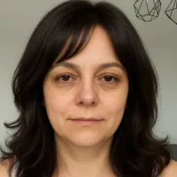 Portret kobiety z ciemnymi włosami i delikatnym uśmiechem, oświetlonej naturalnym światłem, z geometryczną lampą w tle, uchwycony w neutralnym ujęciu.